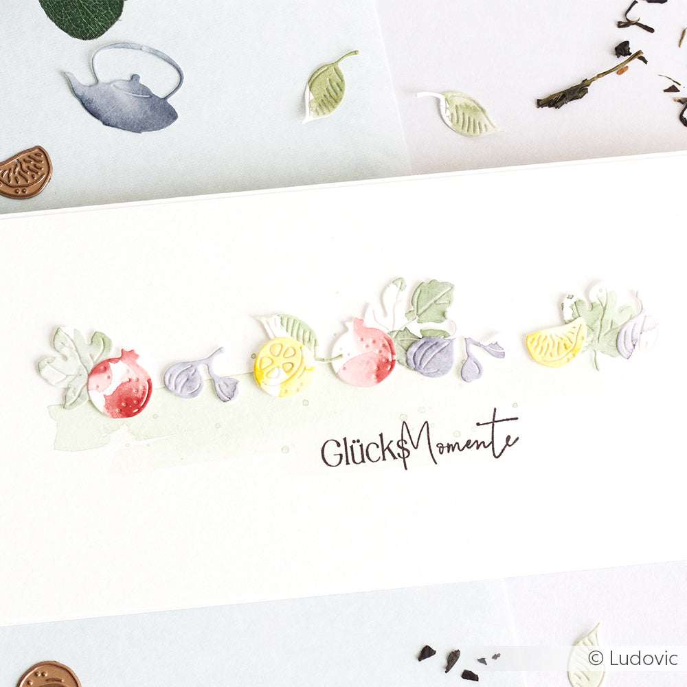 Eine Karte mit farbenfrohen Frucht- und Blattausschnitten, gestaltet mit dem Alexandra Renke Tea time Set, mit "GlücksMomente" in eleganter Schrift.