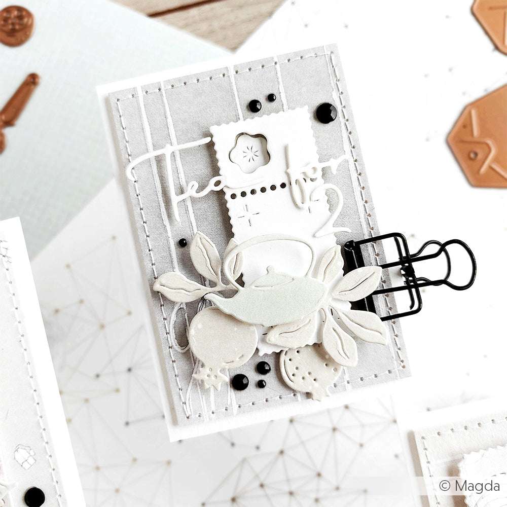 Eine handgefertigte Karte mit geschichteten Papierausschnitten mit Alexandra Renke Stanzen für Designpapier, die ein neutrales Teekannenmotiv zeigt und mit einem schwarzen Binder verschlossen wird.