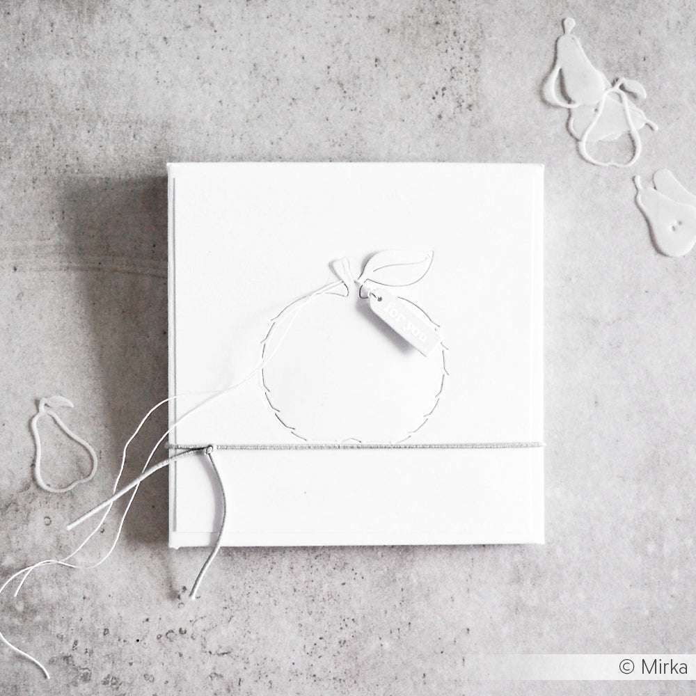 Minimalistische weiße Geschenkbox mit Kordel und birnenförmigem Anhänger, gefertigt von Alexandra Renke Designpapiere mit der Motivstanze Abriss Apfel, dargestellt auf einer hellgrauen, strukturierten Oberfläche.
