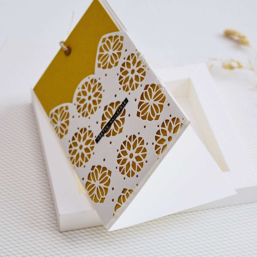 Eine dekorative Karte in Weiß und Gold mit komplizierten Ausstanzungen, die mit der Motivstanze Ornament von Alexandra Renke hergestellt wurden, aufgeschlagen auf einer weißen Schachtel.