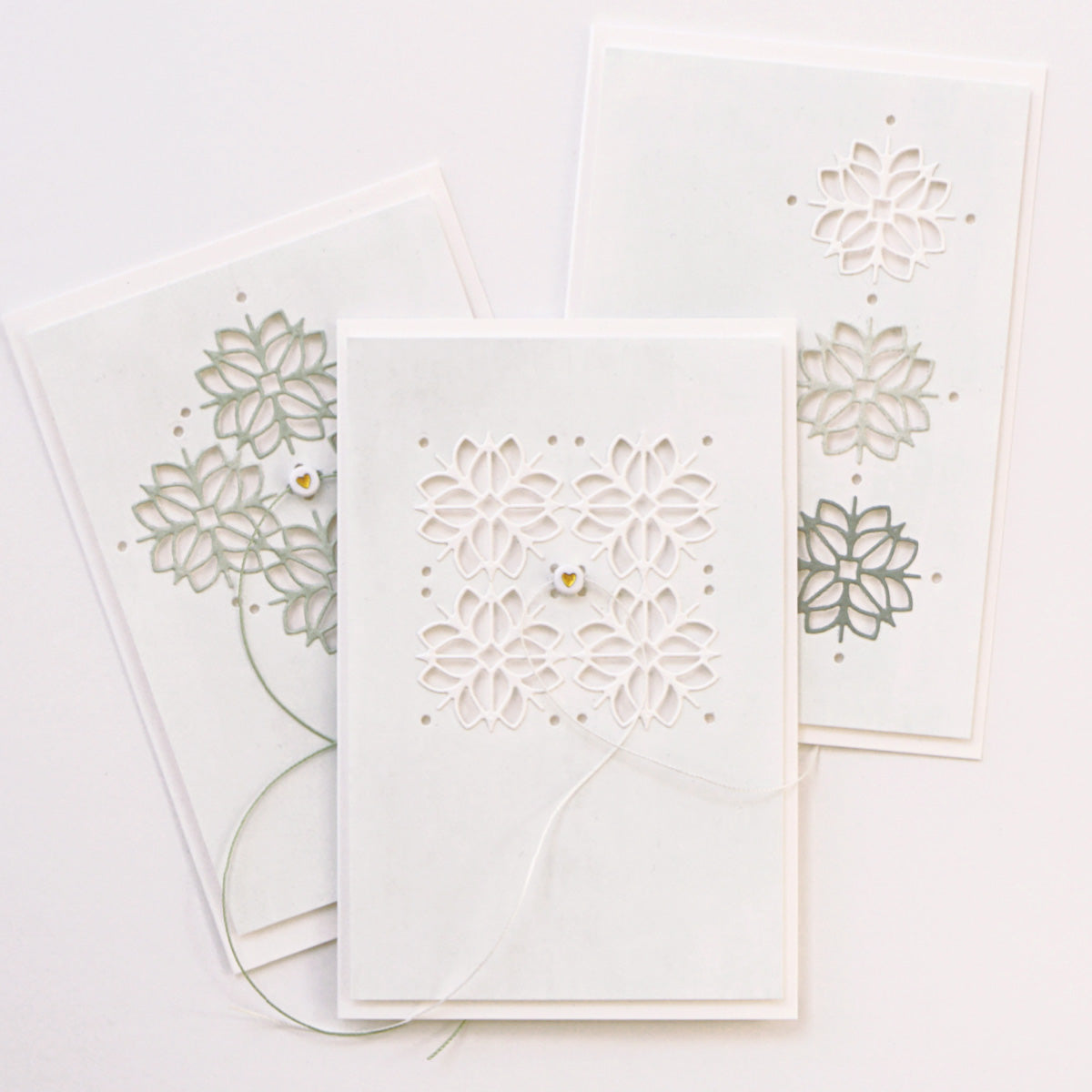 Die drei weißen Grußkarten von Alexandra Renke zeigen aufwendige florale Stanzmotive, die mit DieCut Systemen hergestellt und mit dezentem farbigem Garn akzentuiert wurden.