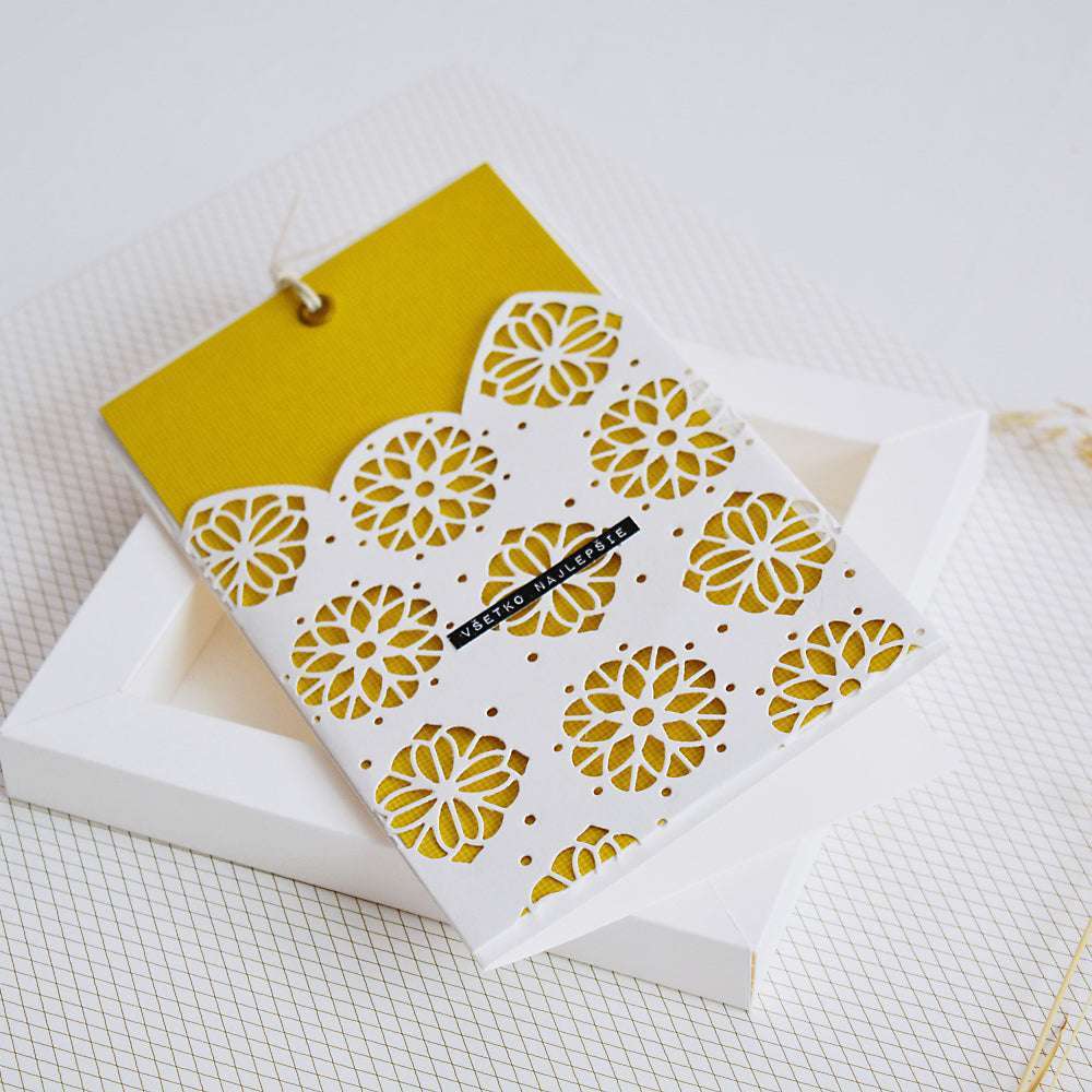 Gelbe und weiße Karte mit floralem Ausschnitt, hergestellt mit Alexandra Renke Motivstanze Ornament mit Kontur, präsentiert auf einer weißen Schachtel mit dezentem Gittermuster.