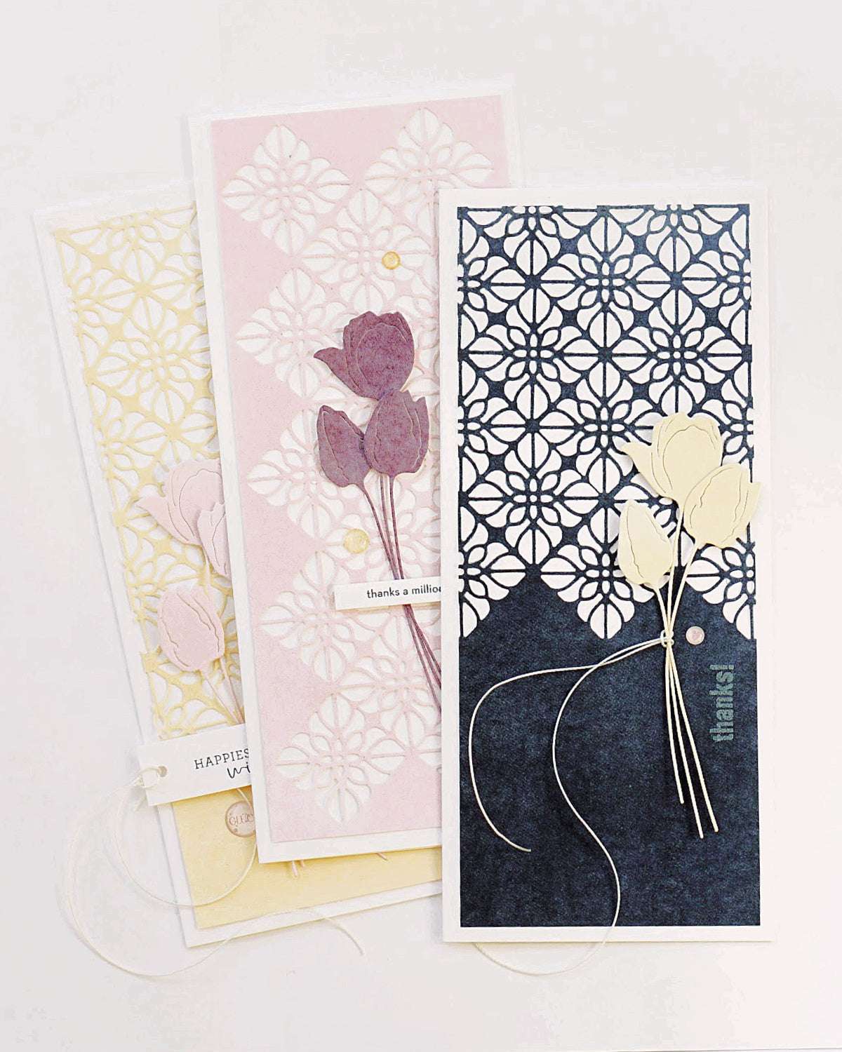 Drei handgefertigte Blumengrußkarten von Alexandra Renke mit Designpapieren und aufwendig ausgeschnittenen Ornamentmotiven auf zart pastellfarbenen Hintergründen, die überlappend dargestellt werden.