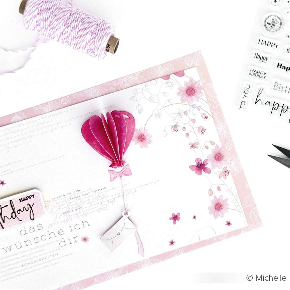 Handgemachte Geburtstagskarte von Alexandra Renke mit rosafarbenen Blumenmustern, einem 3D-Ballon aus Motivstanze Herzballon und einem verzierten Umschlag. Garn und Stempel aus der Nähe sorgen für zusätzlichen Charme.