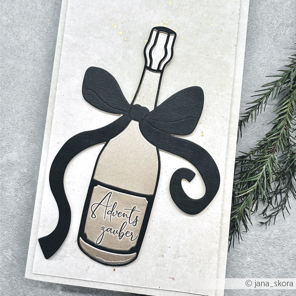 Die festliche Karte von Alexandra Renke zeigt eine Sektflasche mit schwarzer Schleife und Adventszauber"-Etikett, die mit der Motivstanze Große Champagnerflasche als einzigartiges Detail gestaltet wurde.