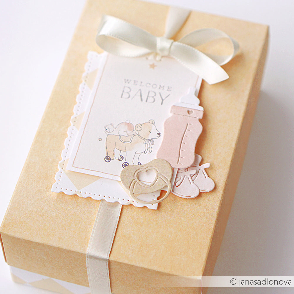 Cremefarbene Geschenkschachtel mit weißem Band, dekoriert mit Alexandra Renke Designpapieren und der Karte Welcome Baby sowie Babyausschnitten aus dem Alexandra Renke Motivstanze Fläschchen Set.