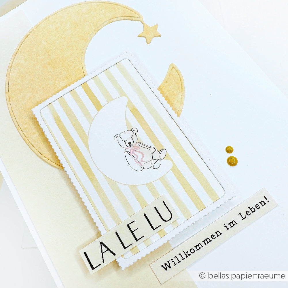 Alexandra Renke Grußkarte mit Mond, Teddybär und den Texten "LALELU" und "Willkommen im Leben!" auf Streifen, hergestellt mit der Motivstanze Mond für zusätzlichen Charme.