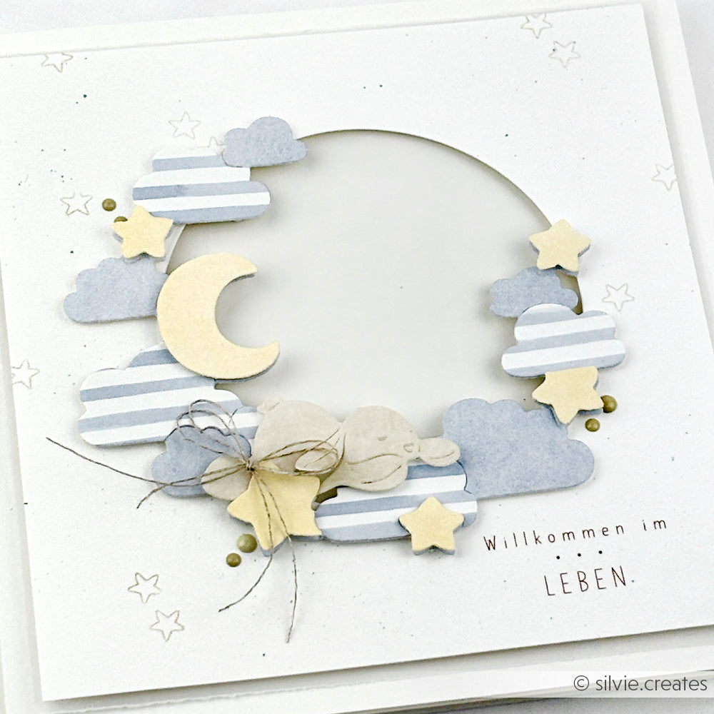 Handgefertigte Karte von Alexandra Renke mit Wolken, Sternen und einem Mond und dem Schriftzug "Willkommen im LEBEN.". Gefertigt mit Motivstanze Nachthimmelkranz und hochwertigen Designpapieren für exquisite, verträumte Details auf weißem Hintergrund.