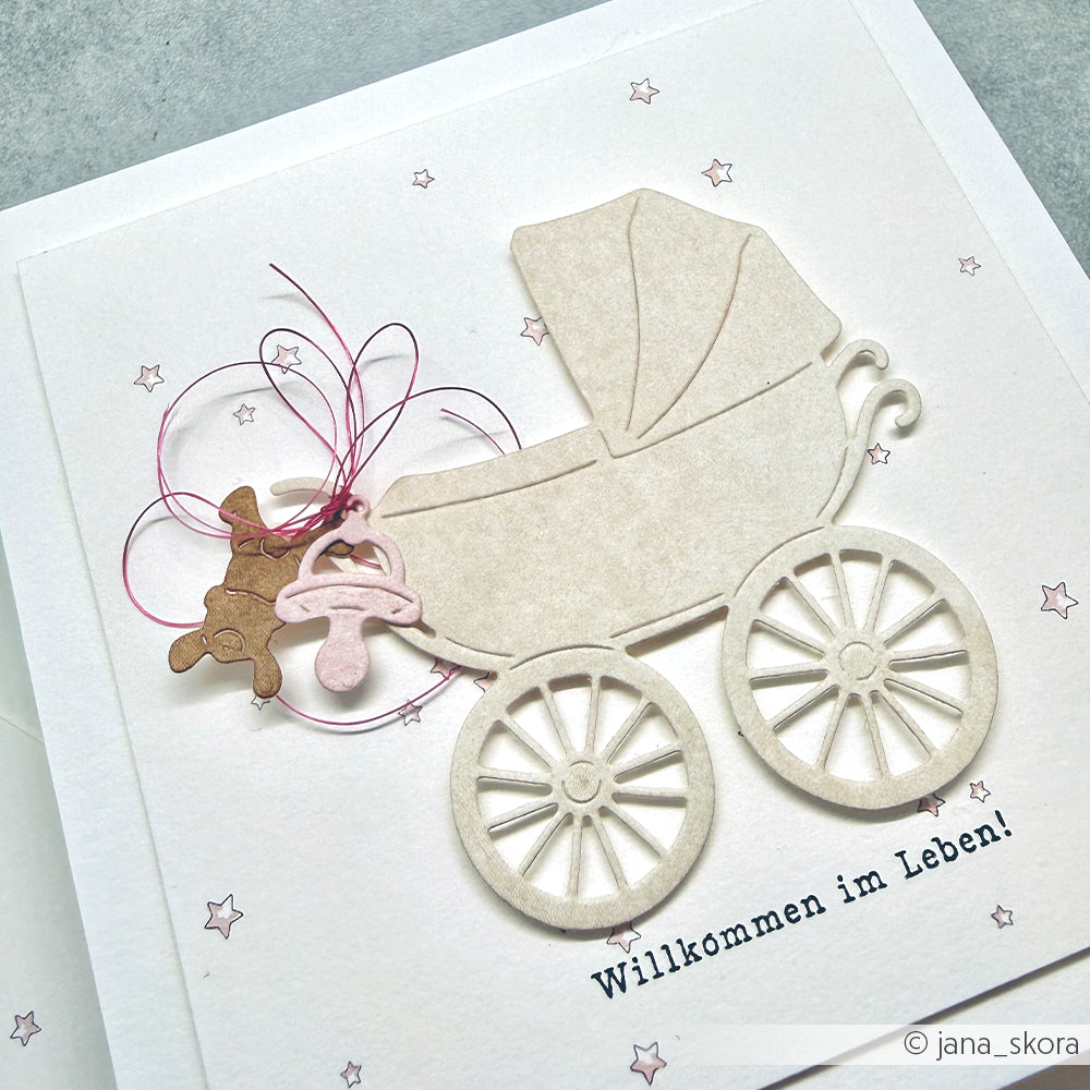 Grußkarte von Alexandra Renke mit Kinderwagen, Schnuller, Teddy und dem Text "Willkommen im Leben!", gestaltet mit Motivstanze Kinderwagen und eleganten Designpapieren für einen charmanten Look.