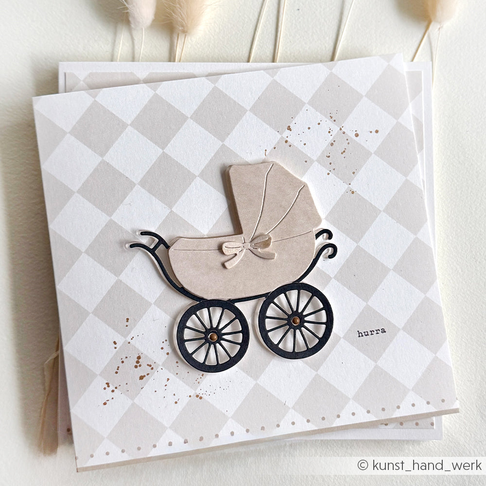 Alexandra Renke-Grußkarte mit einer beigefarbenen Kinderwagen-Illustration, die mit der Motivstanze Kinderwagen auf einem rautenförmigen Hintergrund gestaltet wurde.