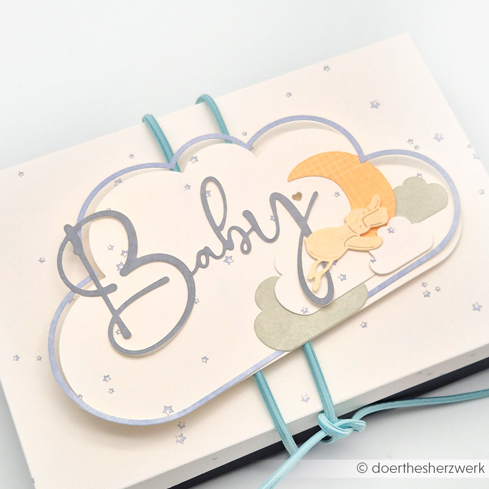 Wolkenförmiges Kärtchen mit dem Text "Baby", einem schlafenden Hasen, Wolken und Mond, hergestellt mit der Motivstanze Kartenaufleger Wolke von Alexandra Renke und gebunden mit blauen Gummibändern. Ideal für kreative Projekte mit DieCut Systemen.