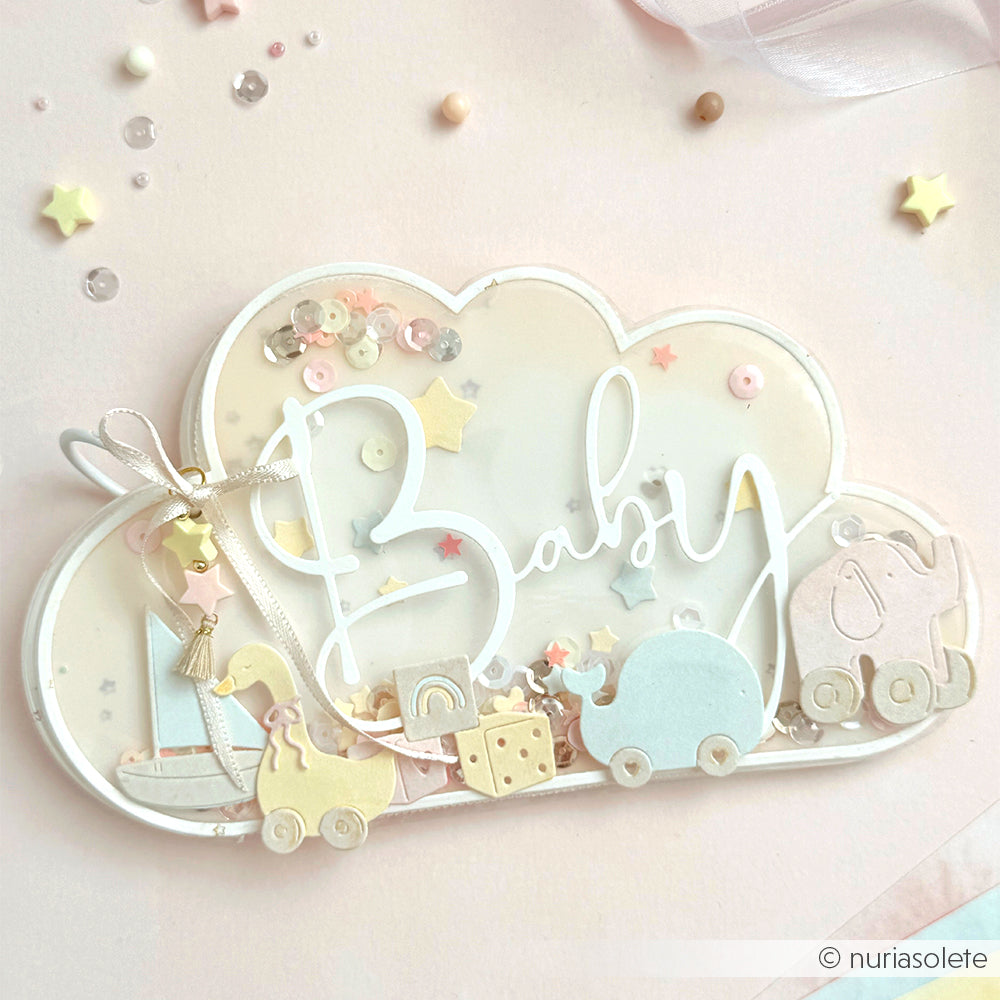Wolkenförmige Karte von Alexandra Renke mit pastellfarbenem Babyspielzeug, Sternen und dem Text "Baby" auf zartrosa Hintergrund - ideal als Motivstanze Kartenaufleger Wolke für Ihr nächstes Designpapiere- oder Stanzsysteme-Projekt.