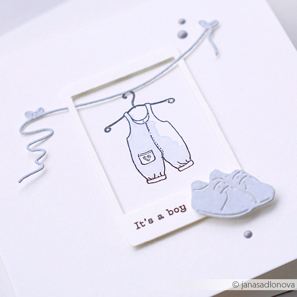 Eine Karte von Alexandra Renke mit einem blauen Babystrampler auf einem Bügel und blauen Babyschuhen, gestaltet mit den Kleine Schuhe Dies, und dem Text "It's a boy".