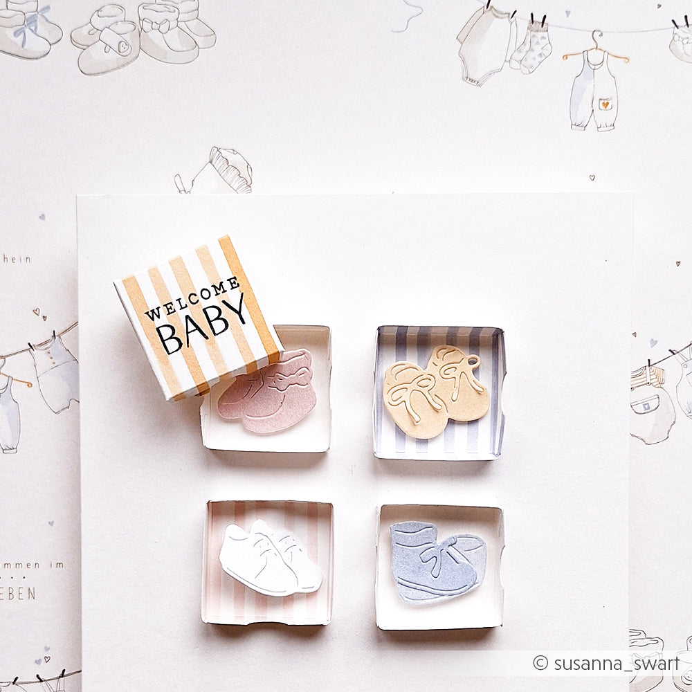 Eine Welcome Baby-Karte von Alexandra Renke mit vier winzigen Babyschuhen aus Papier, die mit der Stanze Kleine Schuhe hergestellt wurden, angeordnet in pastellfarbenen Kästchen auf einem weißen Hintergrund.