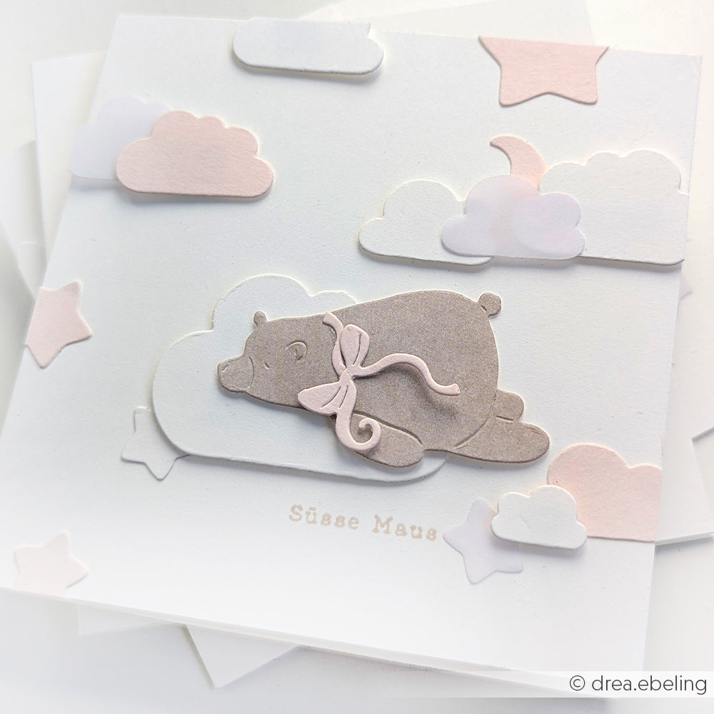 Eine pastellfarbene Grußkarte von Alexandra Renke mit einem Bären auf einer Wolke mit Sternen und zartrosa und weißen Akzenten - ideal für die Kombination mit Motivstanze oder Designpapieren, um Ihren Kreationen eine einzigartige Note zu verleihen.