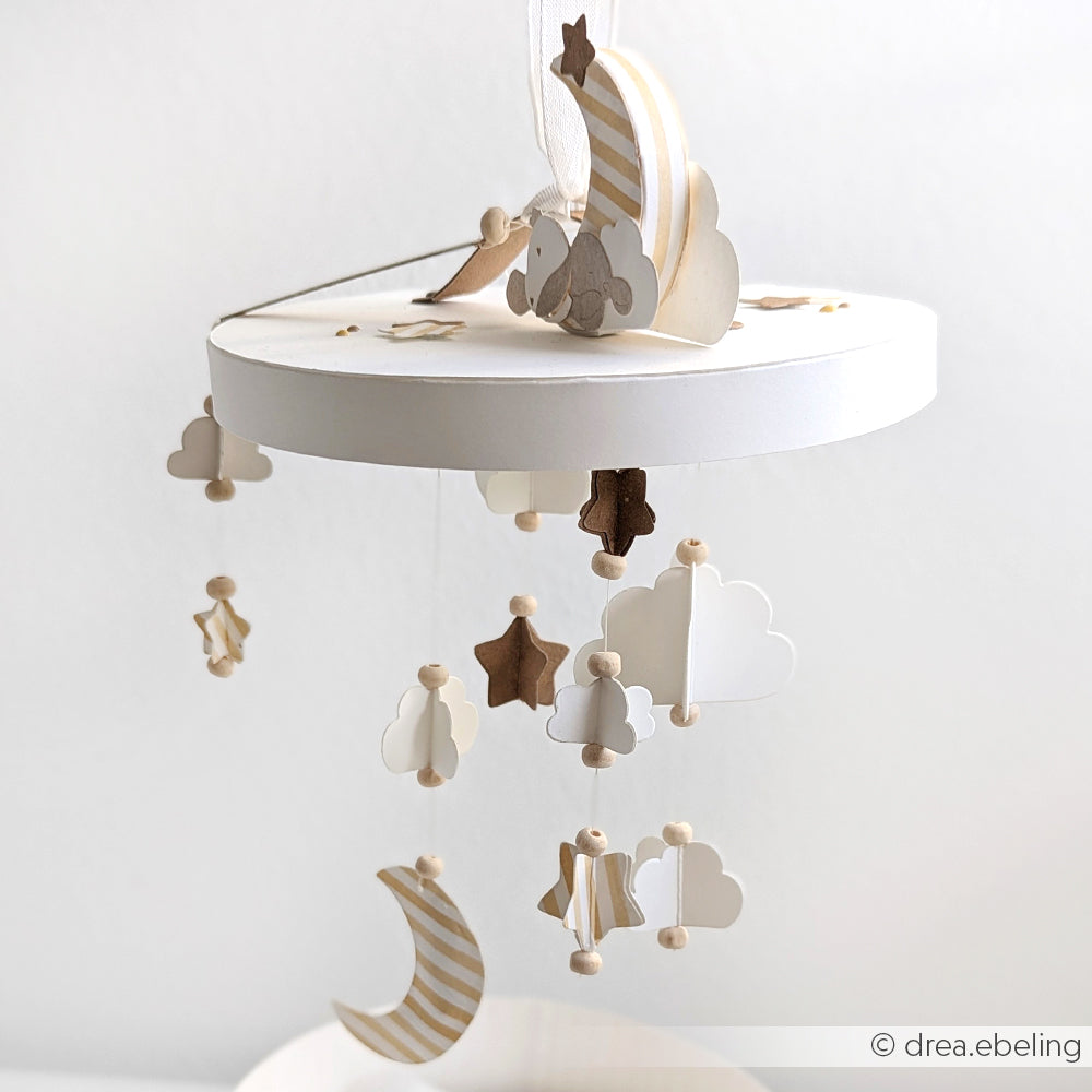 Das in neutralen Tönen gehaltene Baby-Mobile von Alexandra Renke zeigt Wolken, Sterne und eine Mondsichel auf einem runden, weißen Rahmen - gefertigt aus Designpapieren für zarte Formen und akzentuiert mit Traumkonfetti für einen verträumten Effekt.
