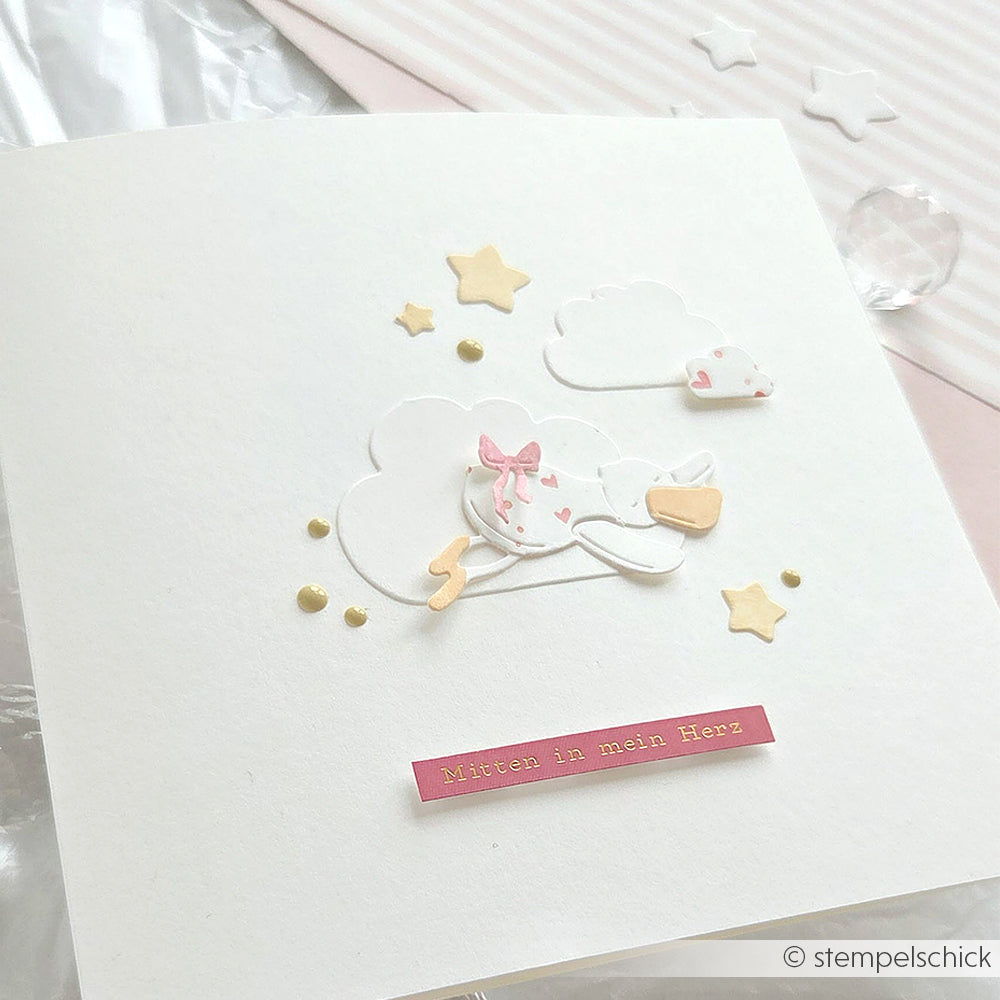 Handgefertigte Alexandra Renke Karte mit Storch, Sternen, Wolken und dem Text "Mitten in mein Herz" auf weißem Hintergrund, hergestellt mit Motivstanze und hochwertigen Designpapieren für eine einzigartige Note.
