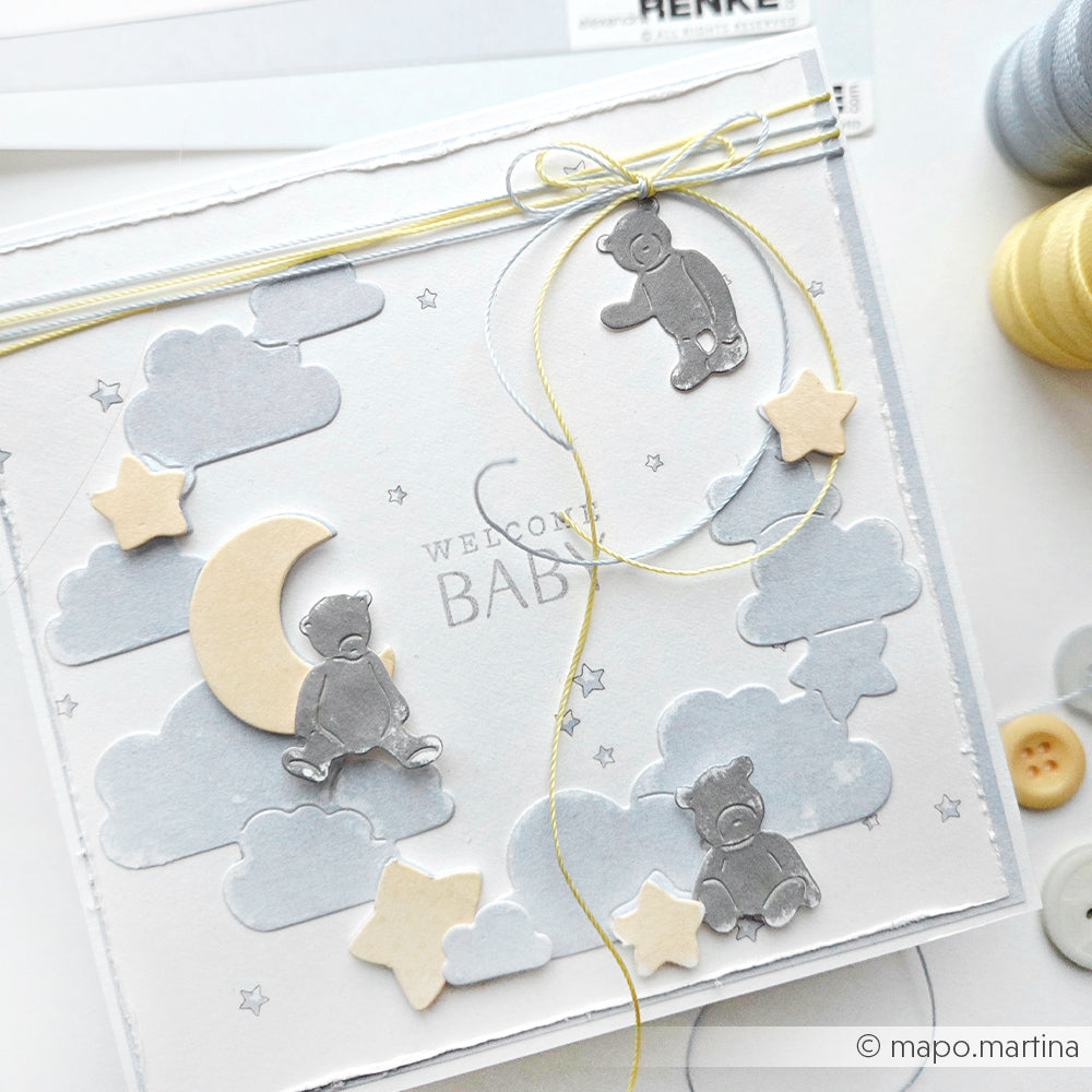 Handgefertigte Babykarte von Alexandra Renke, hergestellt aus Designpapier mit Wolken, Sternen, Teddybären, Mond und dem Text "Welcome Baby". Mit einer Motivstanze verziert und mit gelber Kordel verziert.