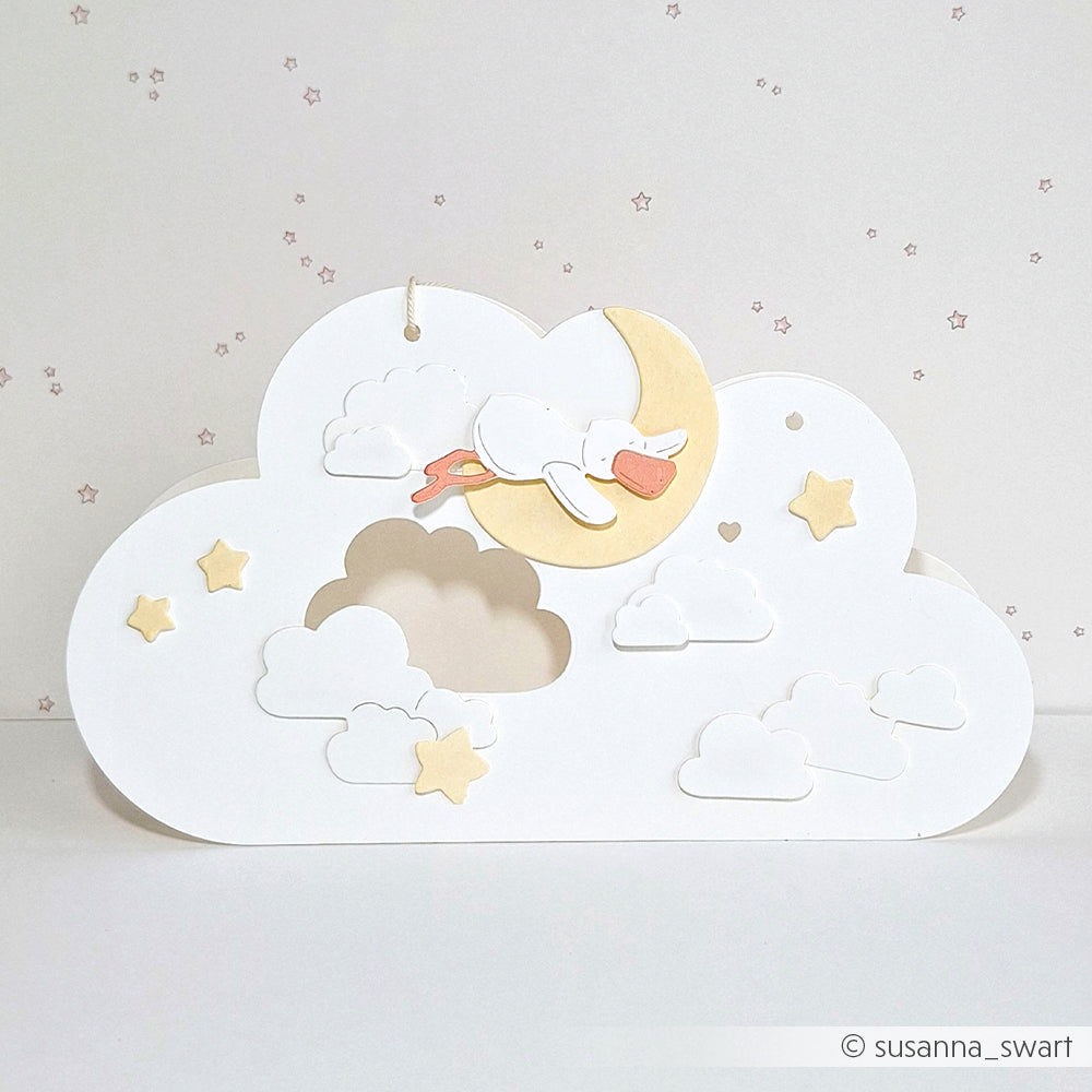 Ein Storch fliegt über einen Mond mit Wolken und Sternen auf weißem Grund, gestaltet mit feinen Alexandra Renke Designpapieren und präziser Motivstanztechnik.