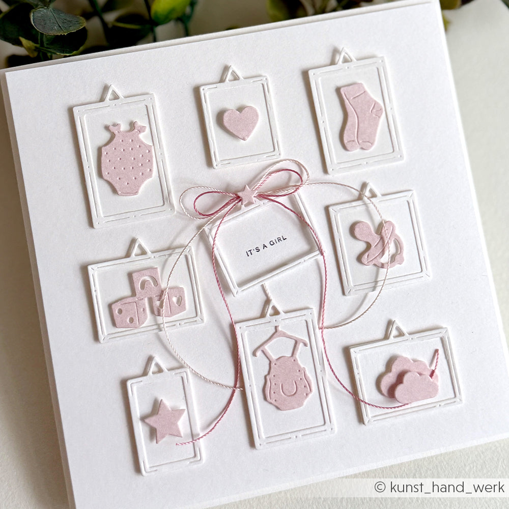 Eine handgefertigte "It's a Girl"-Karte von Alexandra Renke zeigt rosafarbene Stanzteile mit Babymotiven, die auf einem strahlend weißen Hintergrund wunderschön eingerahmt sind.