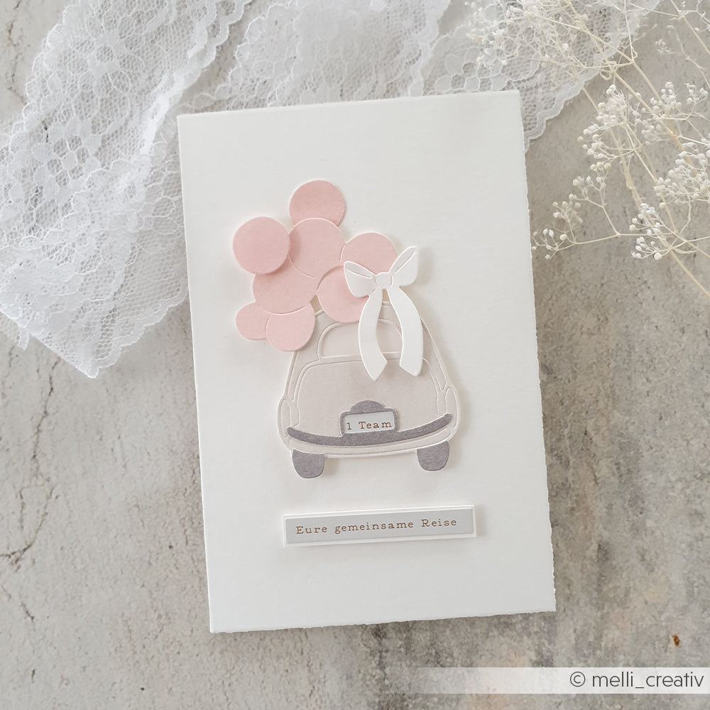 Handgemachte Karte von Alexandra Renke, gestaltet mit Spezialpapier, mit einem Auto, rosa Luftballons und einer weißen Schleife; deutscher Text: "Eure gemeinsame Reise.