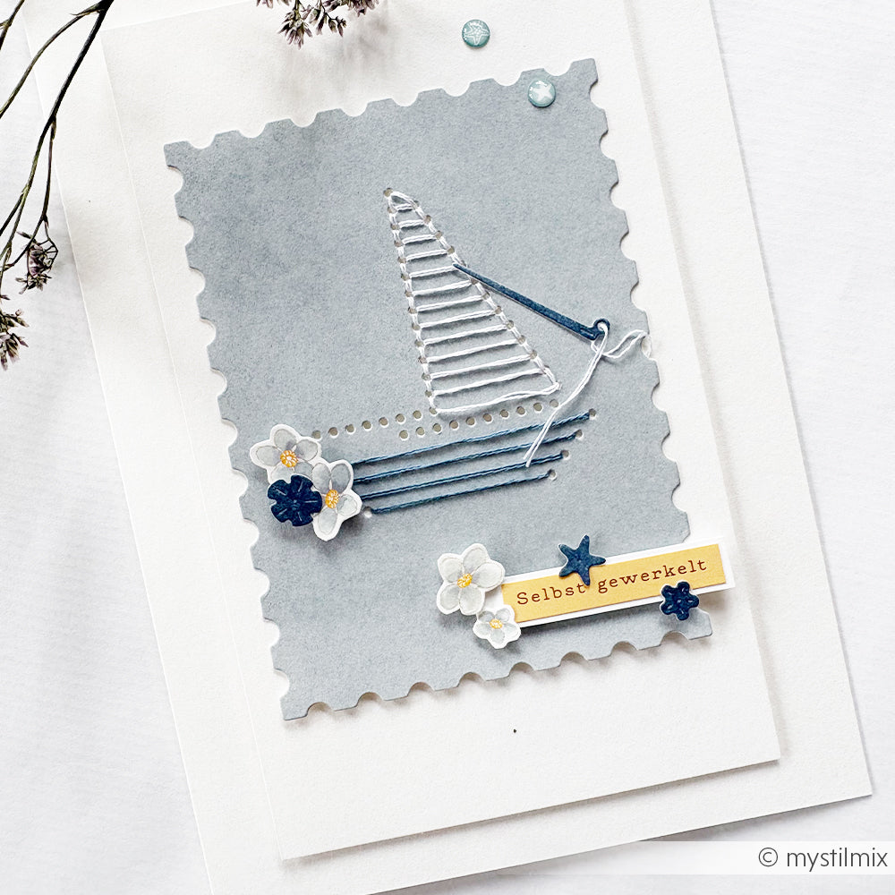 Eine handgefertigte Postkarte von Alexandra Renke mit gesticktem Schiff, zarten Blumen, einem „Selbst gewerkelt“-Etikett und grauem Designpapier – kunstvoll gestaltet mit einer Motivstanze.