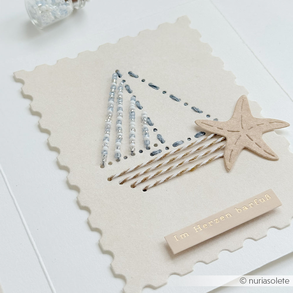 Handgefertigte Karte von Alexandra Renke mit Fadenkunst in Dreiecksform, verziert mit einem Seestern-Motiv und einem Etikett mit der Aufschrift „Im Herzen barfuß“ – gefertigt aus erlesenen Designpapieren von Alexandra Renke und präzise mit Details aus der Motivstanze veredelt.