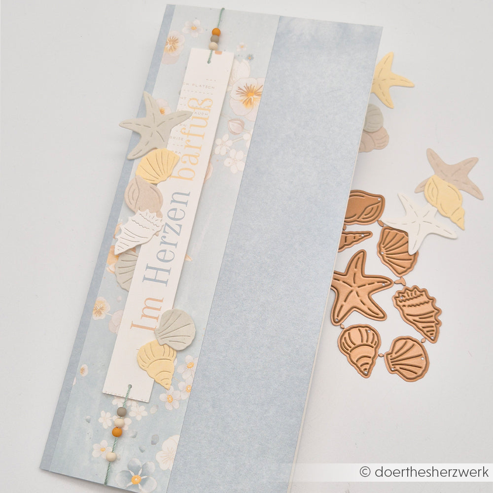 Eine Pastellkarte mit Muschel- und Seestern-Ausschnitten, die mit dem „Kleines Muschel Set“ von Alexandra Renke Motivstanze gestaltet wurde, mit deutschem Text und dekorativen Designpapier-Elementen, präsentiert auf weißem Hintergrund.