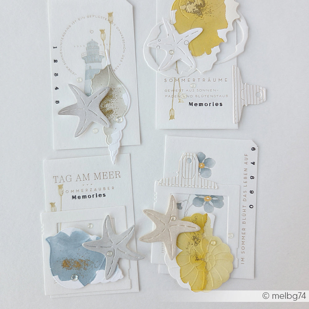 Fünf handgefertigte Karten von Alexandra Renke mit Seesternen, Muscheln, Blumen und deutschem Text, angeordnet auf weißem Hintergrund. Jedes Motiv besticht durch filigrane Details, die mit „Stanzen aus Stahl“ und der Motivstanze „Kleines Muschel-Set“ gestaltet wurden – perfekt für alle Fans von DieCut-Systemen.