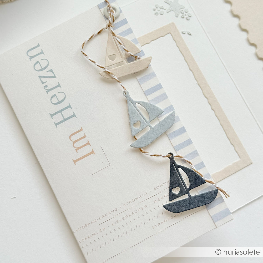 Drei kleine Segelboot-Ausschnitte, die aus Designpapieren von Alexandra Renke und mit einer Motivstanze „Maritime Anhänger Die“ gefertigt wurden, sind an einer Schnur auf einer schlichten Karte mit deutschem Text und sanften, neutralen Farben angebracht.