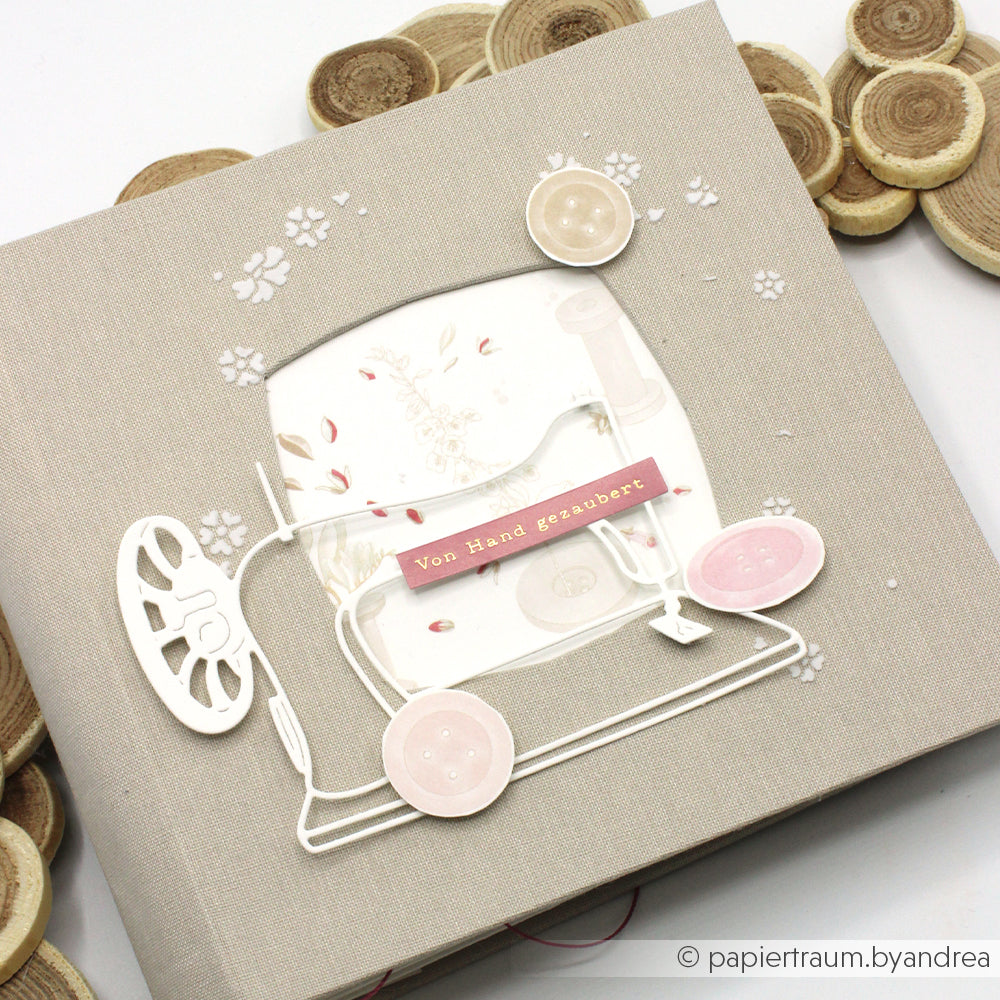 Handgefertigtes Scrapbook von Alexandra Renke mit einem Motiv eines weißen Kinderwagens, hergestellt aus hochwertigen Designpapieren und mit einem „Von Hand gemacht“-Etikett auf dem beigen Einband.
