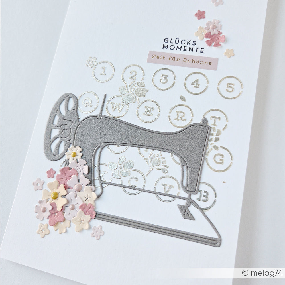 Eine Karte von Alexandra Renke mit einer Nähmaschinenillustration, pastellfarbenen Blumen und einem deutschen Text mit Zahlen im Vintage-Stil, gestaltet aus Designpapieren und mit der Motivstanze „Nähmaschine“ für zusätzliche Details.
