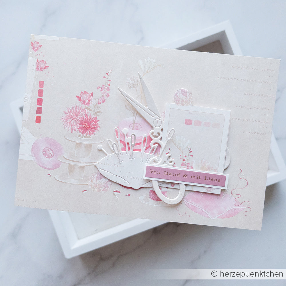 Eine handgefertigte Karte von Alexandra Renke mit rosa Verzierungen zum Thema Nähen, verziert mit Designpapier-Akzenten und dem deutschen Text „Von Hand & mit Liebe“.