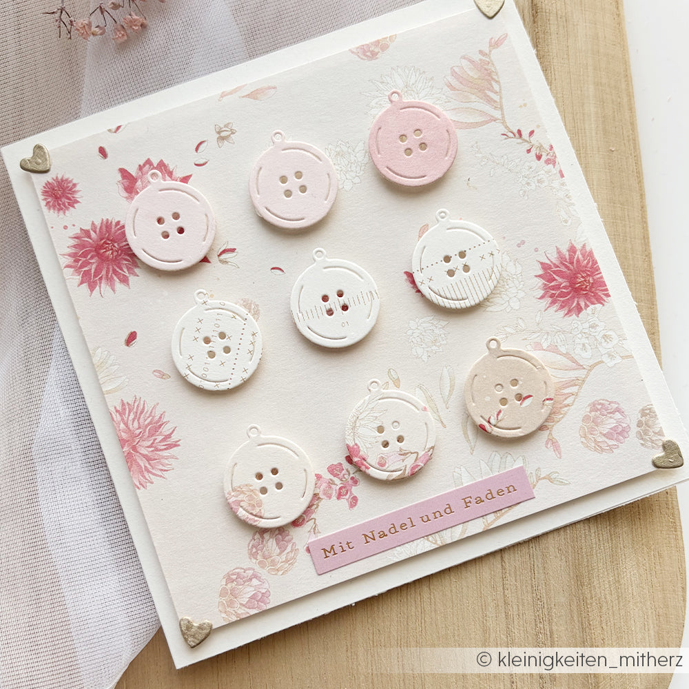 Eine handgefertigte Karte von Alexandra Renke mit neun dekorativen Knopfmotiven und Blumenmustern in Rosa und Creme, hergestellt aus hochwertigem Designpapier und mit zarten Motivstanzungen für eine einzigartige Note.