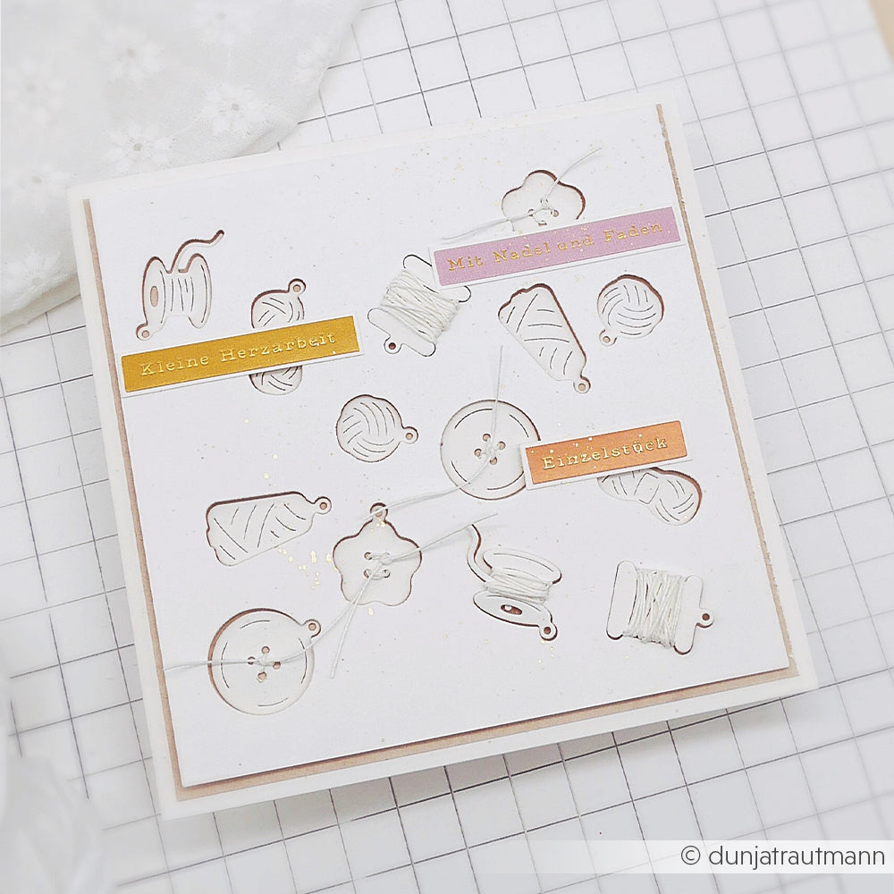 Eine handgefertigte Karte aus Designpapieren von Alexandra Renke und mit der Motivstanze „Spaß mit Wolle“, verziert mit Ausschnitten zum Thema Nähen, Akzenten aus weißem Garn, deutschen Sprüchen und einem karierten Hintergrund.