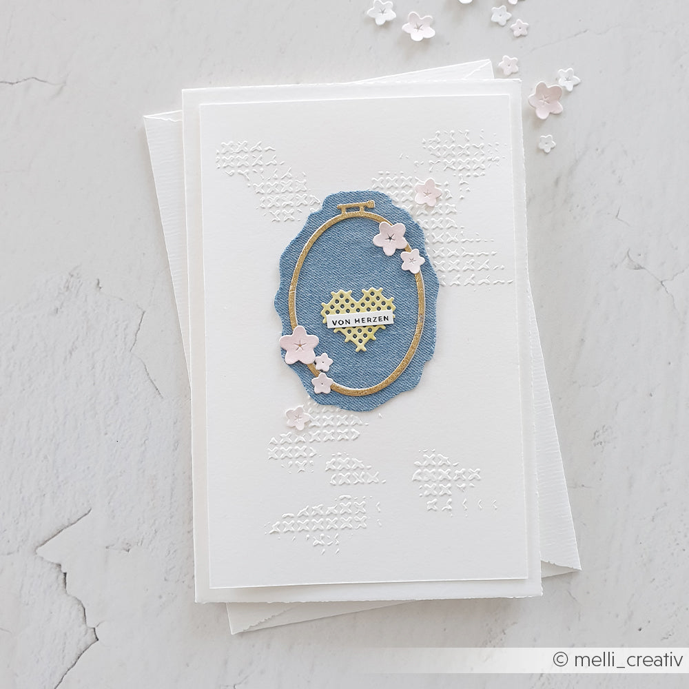 Handgefertigte weiße Karte aus Designpapieren von Alexandra Renke mit einem blauen, bestickten ovalen Rahmen (Motivstanze „Stickrahmen Oval“), rosa Blumen und einem Herz mit der Aufschrift „VON HERZEN“ in der Mitte.