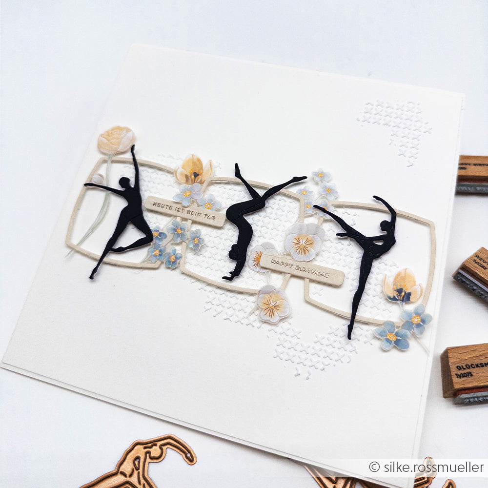 Handgefertigte Karte von Alexandra Renke mit Ballerina-Silhouetten, blauen und beigen Blumen, deutschem Text und zarten Details aus Designpapier auf strahlend weißem Hintergrund.