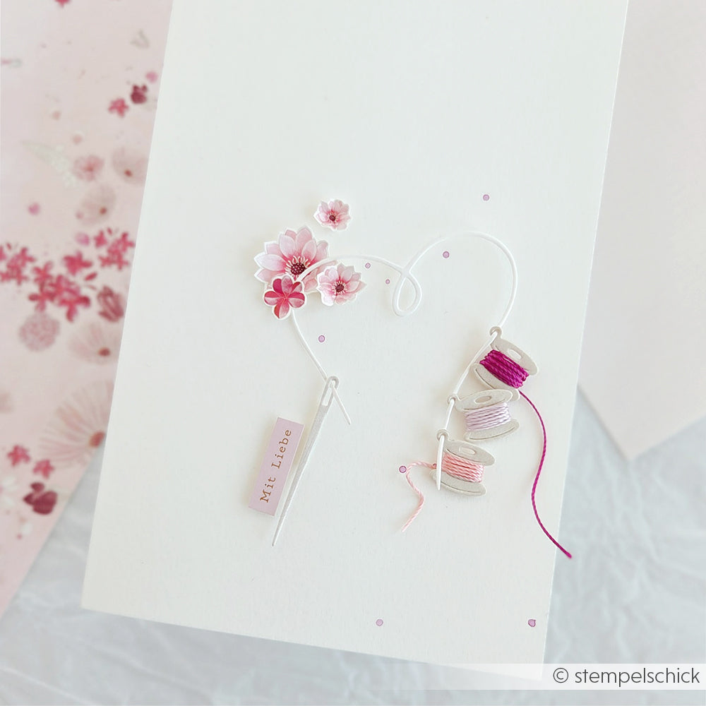 Handgefertigte Karte mit rosa Blumen, herzförmigem Draht und rosa Garnspulen auf weißem Hintergrund, gestaltet mit Designpapieren von Alexandra Renke und einer Motivstanze für einzigartige Details.