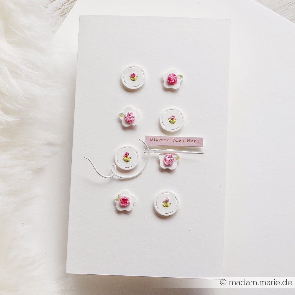 Diese weiße Karte von Alexandra Renke ist mit kleinen rosa und weißen Blumen verziert, die mit einer Motivstanze auf feinem Designpapier ausgestanzt wurden, und mit einem „Blumen fürs Herz“-Etikett veredelt.