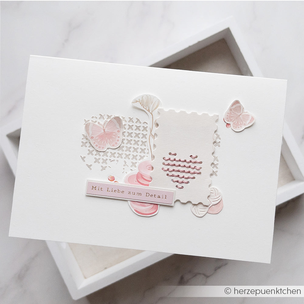 Weiße Karte von Alexandra Renke mit rosa und beigen Schmetterlingen, abstrakten Formen und dem Schriftzug „Mit Liebe zum Detail“ auf Deutsch. Mit Stanzen für Designpapier und DieCut-Systemen gestaltet, um ihr eine einzigartige, detailreiche Note zu verleihen.