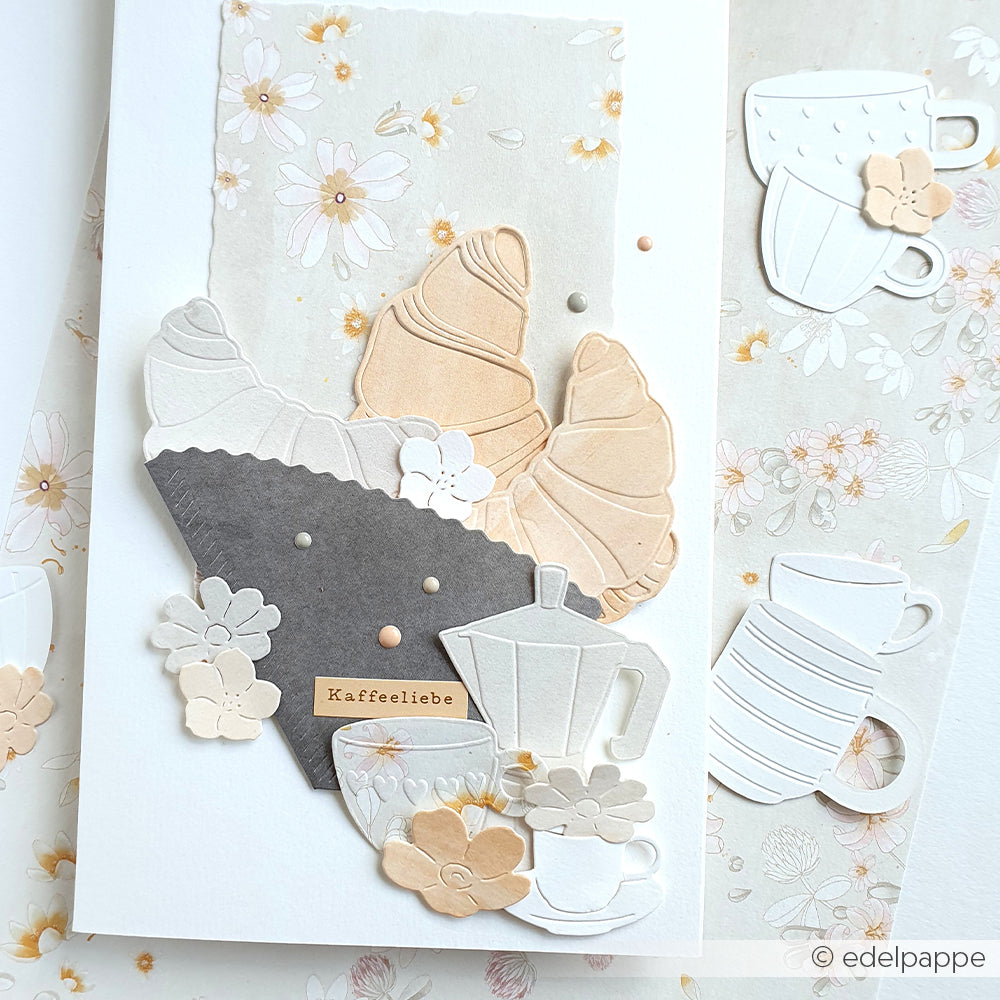 Handgefertigte Karte mit Designpapier von Alexandra Renke, Croissants, die mit dem „Motivstanze Croissant Outline DieCut System“ ausgestanzt wurden, Kaffeetassen, Blumen und dem Schriftzug „Kaffeeliebe“ auf einem blumigen Hintergrund.