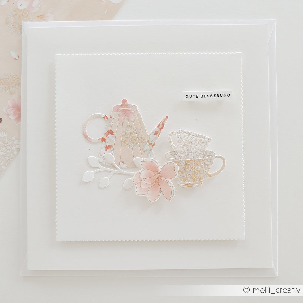 Handgefertigte Karte von Alexandra Renke mit einer pastellfarbenen Teekanne, Tassen, Blumen und dem Schriftzug „Gute Besserung“ auf weißem Hintergrund, gestaltet mit Designpapieren von Alexandra Renke und der Motivstanze „Blumiges Teeset“ für reizvolle Details.