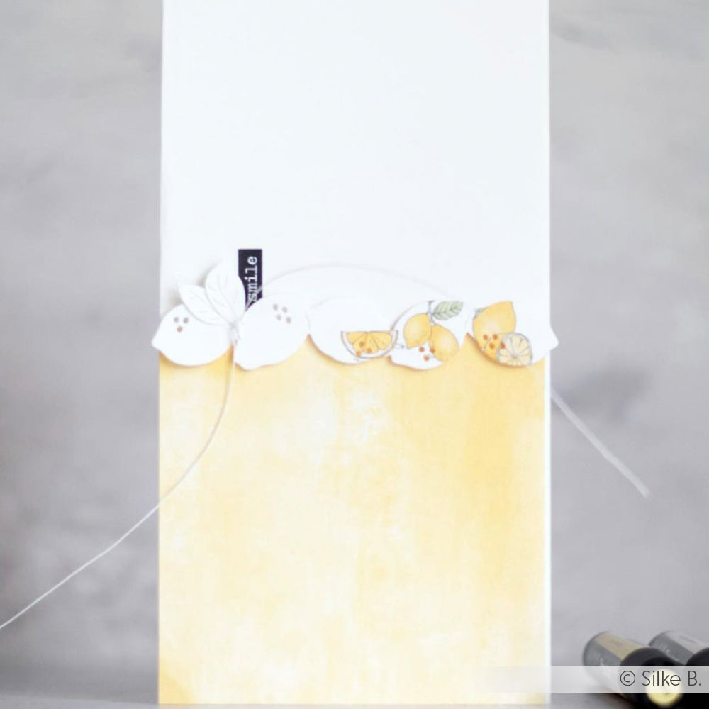 Eine weiß-gelbe Karte mit illustrierten Zitronen und Blättern auf der Oberseite, die mit der Alexandra Renke Motivstanze Zitronen Reihe eine charmante Note erhält.