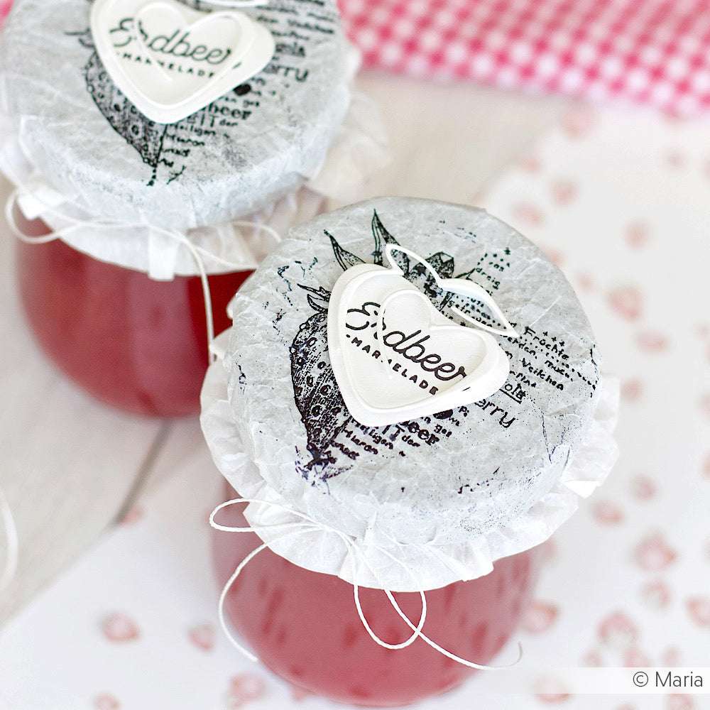 Zwei Gläser Erdbeermarmelade mit dekorativen Deckeln und herzförmigen Etiketten, hergestellt mit der Alexandra Renke Motivstanze Erdbeere.