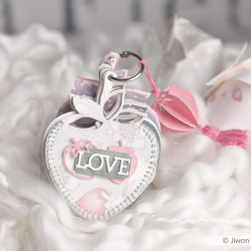 Ein herzförmiger Schlüsselanhänger von Alexandra Renke mit der Aufschrift LOVE in zarten Rosa- und Weißtönen - ideal als süßes Accessoire oder für charmante Geschenkanhänger aus Designpapieren.