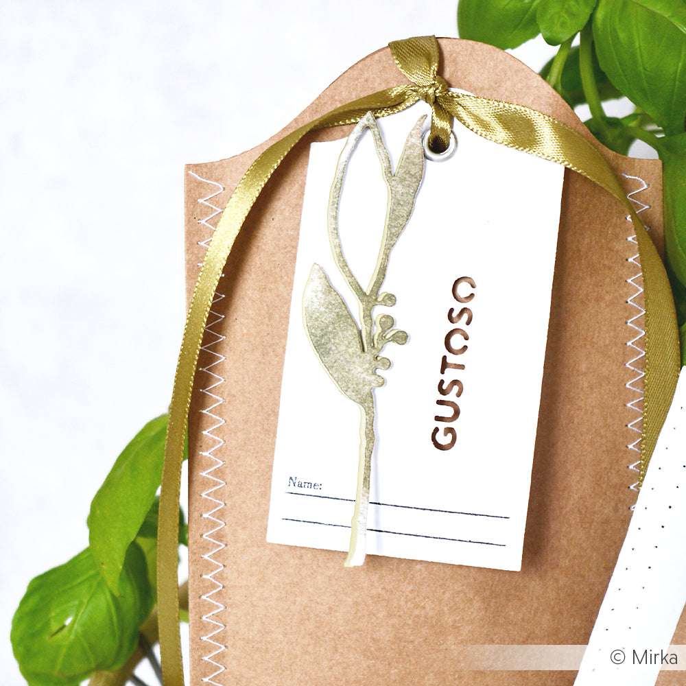 Geschenkanhänger mit goldenem Band, Blattillustration von Alexandra Renke Motivstanze Lorbeer und Text GUSTOSO, befestigt an einer braunen genähten Verpackung.