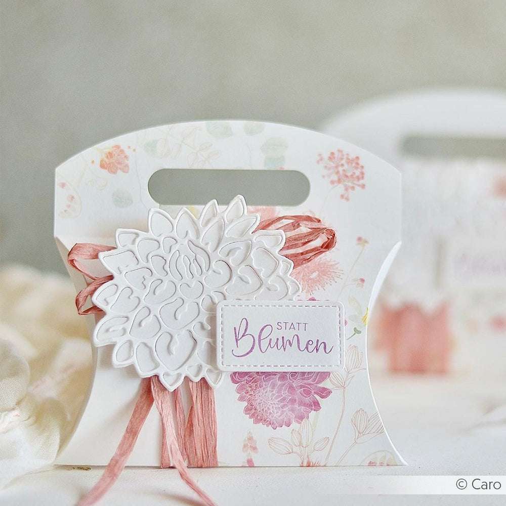 Dekorative florale Geschenkbox mit rosafarbenem Band und einem Statt Blumen Anhänger, gestaltet mit Alexandra Renke Designpapieren und veredelt mit der Motivstanze Dahlienblüte DieCut Systeme auf hellem Hintergrund.
