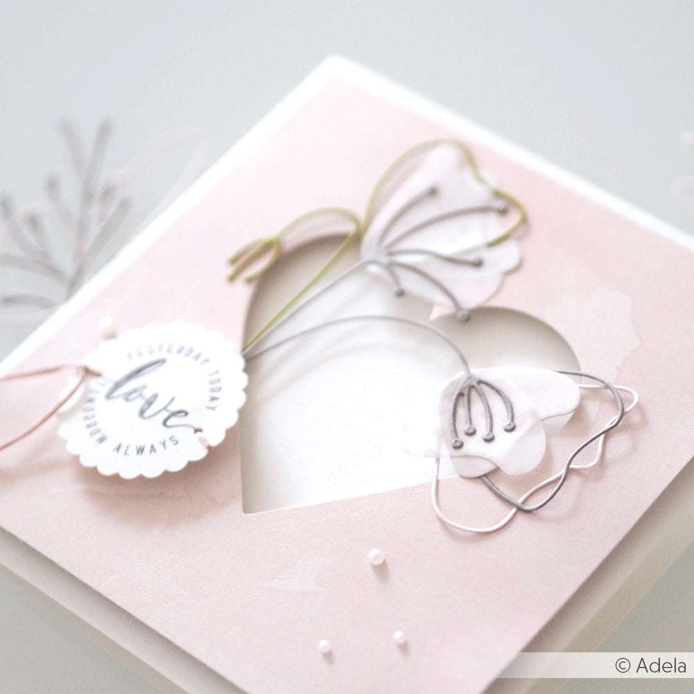 Handgefertigte Karte in Pastellrosa von Alexandra Renke, gestaltet mit Designpapier und Herzausschnitt, verziert mit floralen Akzenten, die mit der Motivstanze Artistblumen gestanzt wurden, und vervollständigt mit einem Anhänger "Liebe für immer".