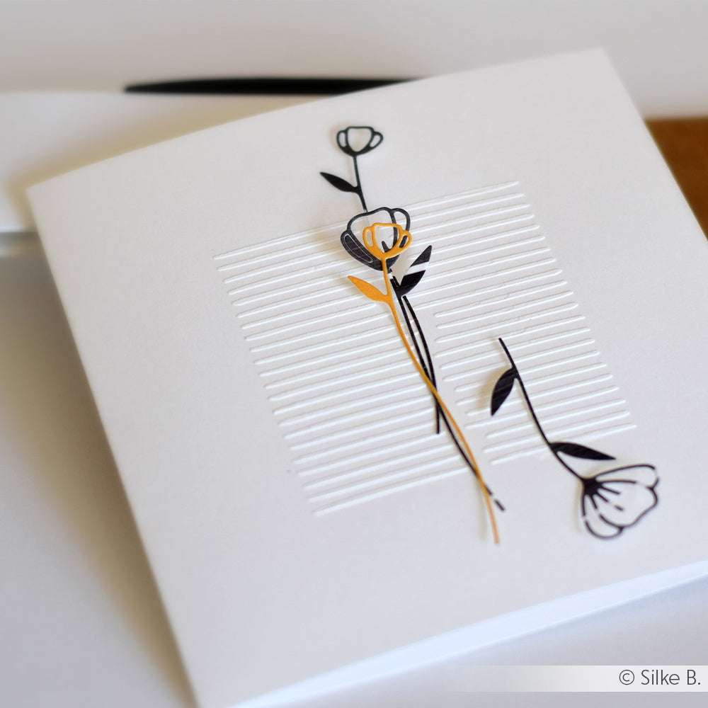 Minimalistische weiße Karte mit geprägten Linien und zwei schlichten schwarzen und gelben Blumenmustern, die mit der Motivstanze Artistblumen von Alexandra Renke hergestellt wurden und für ein elegantes Finish sorgen.