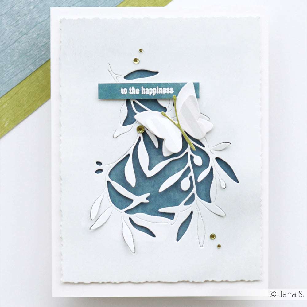 Elegante weiße Karte von Alexandra Renke mit einer blauen Blattstanze (Motivstanze Olivenzweig), einem zarten weißen Schmetterling und dem Spruch "Zum Glück" auf der Vorderseite.
